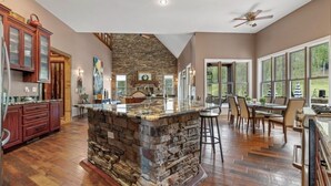 Una cocina amplia con una isla de piedra, armarios de madera y grandes ventanales con vistas al exterior.