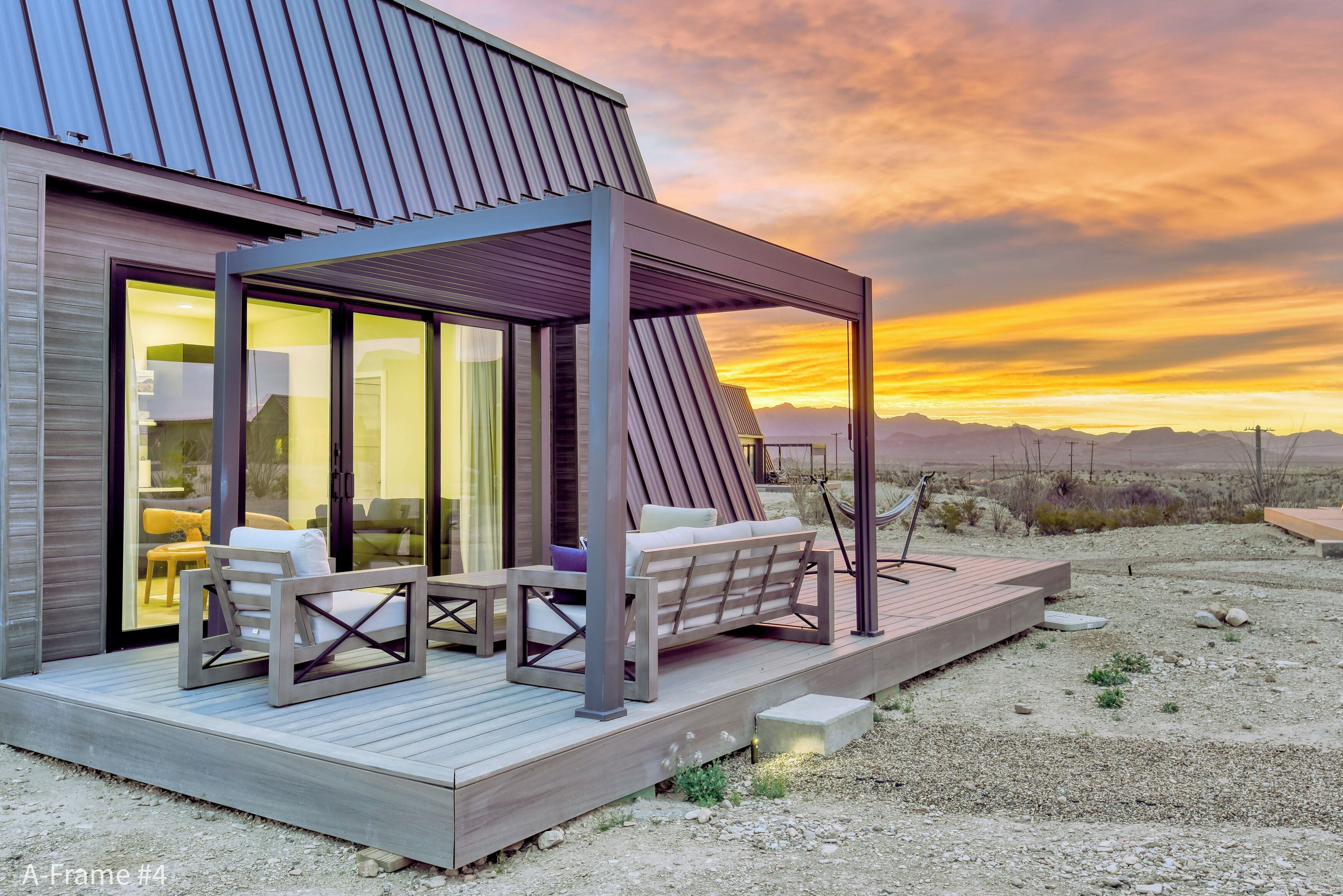 Een moderne buitenruimte met een houten terras, een overdekte zithoek en uitzicht op de zonsondergang.