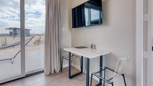 Une chambre moderne avec une table blanche, deux chaises, un téléviseur fixé au mur et une grande fenêtre donnant sur un bâtiment et un paysage.