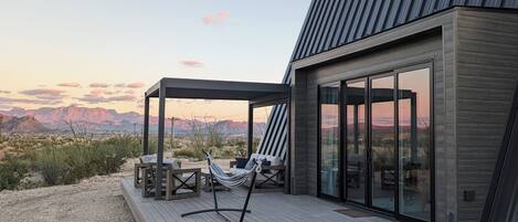Una casa moderna con terraza, hamaca y vistas a las montañas.