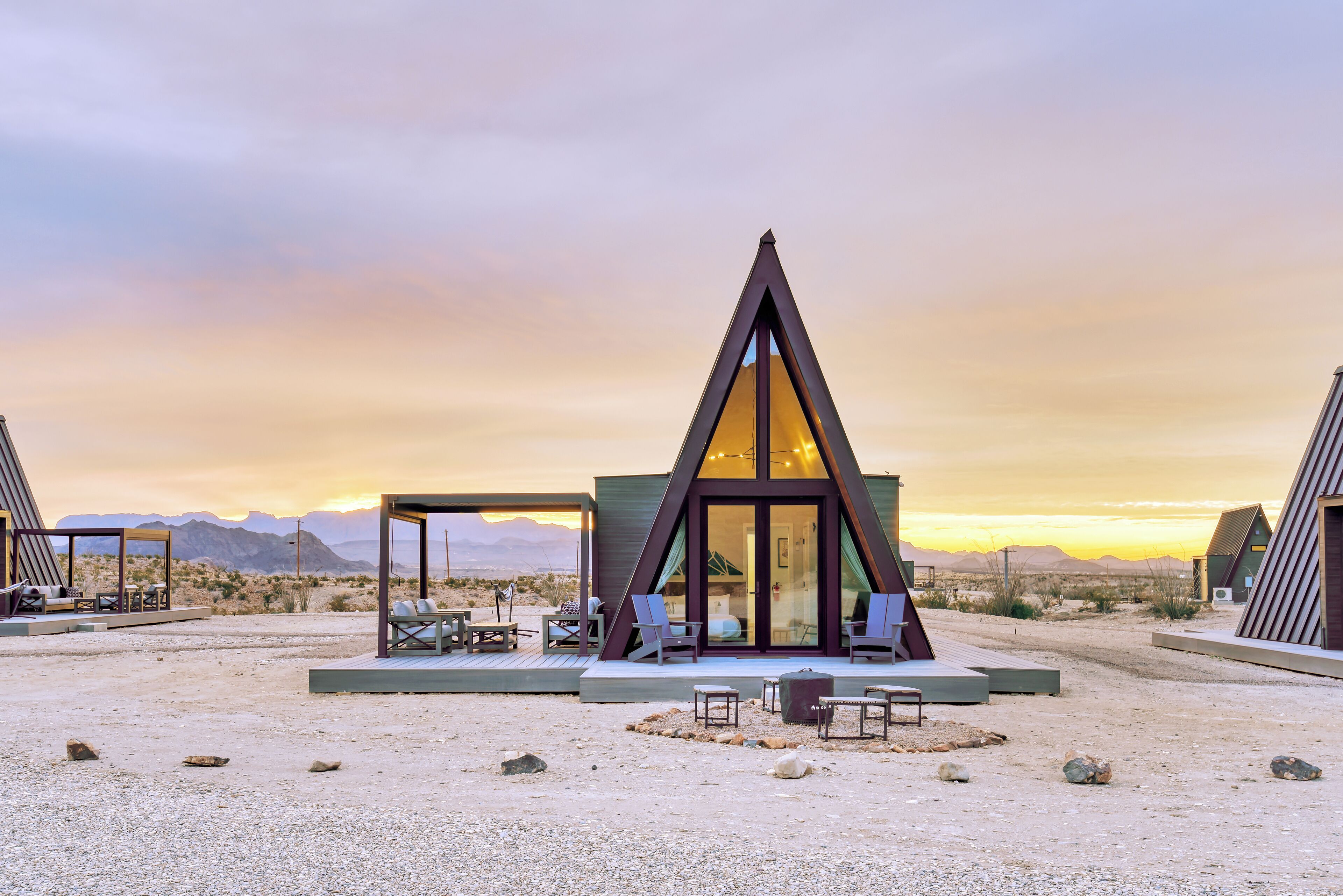 Un edificio moderno de forma triangular con entrada de vidrio, zona de estar al aire libre y un paisaje desértico de fondo.