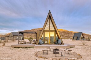 A modern A-frame building with a patio area, outdoor seating, and a fire pit. - Stardust Big Bend Luxury A-Frames (Terlingua)
