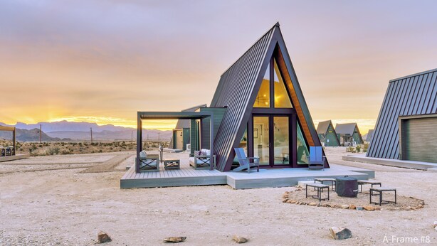 Un bâtiment moderne de forme triangulaire, doté d’une façade en verre, situé dans un paysage désertique avec des montagnes en arrière-plan.