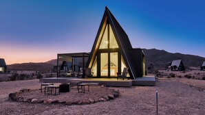 Un bâtiment moderne de forme triangulaire, doté d’une façade en verre, d’un espace extérieur aménagé pour s’asseoir et offrant une vue sur le paysage désertique environnant.