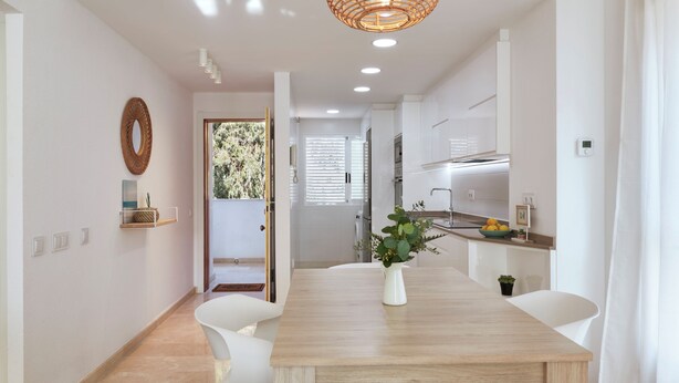 Une cuisine moderne avec des meubles blancs, une table à manger en bois et un luminaire suspendu.