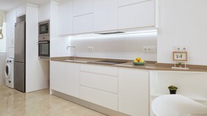 Une cuisine moderne avec des meubles blancs, un réfrigérateur en acier inoxydable, un four, un four à micro-ondes et un évier. On aperçoit une petite plante et un tableau encadré sur le plan de travail.