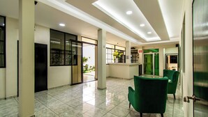 Eine geräumige Lobby mit hoher Decke, gefliestem Boden und grünen Stühlen.