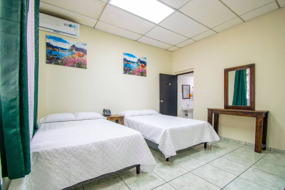 Een hotelkamer met twee bedden, een houten nachtkastje, een spiegel en twee aan de muur gehangen schilderijen.