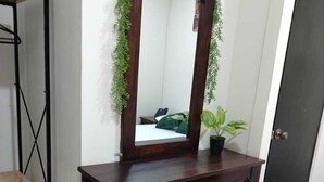Ein Schlafzimmer mit einem Holztisch, einem Stuhl, einem Bett, einer Tür und einer kleinen Topfpflanze.