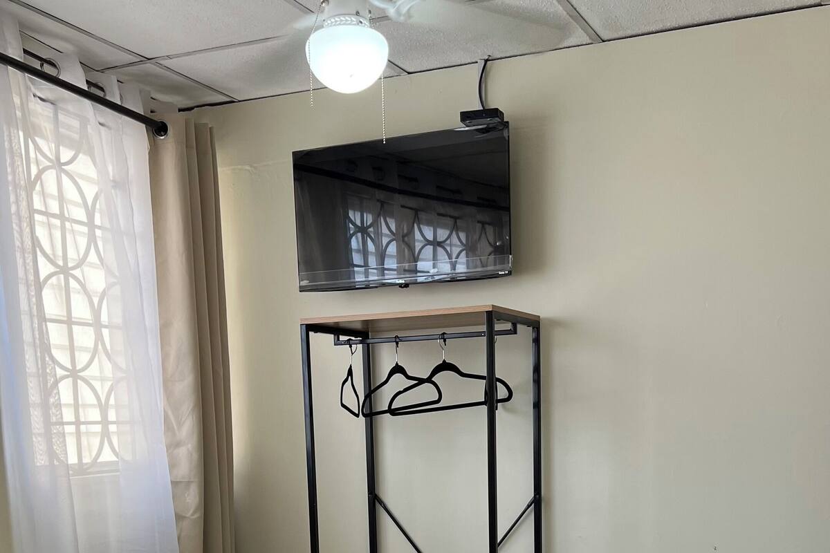 Een hotelkamer met een bed, nachtkastje, tv aan de muur en een plafondventilator.