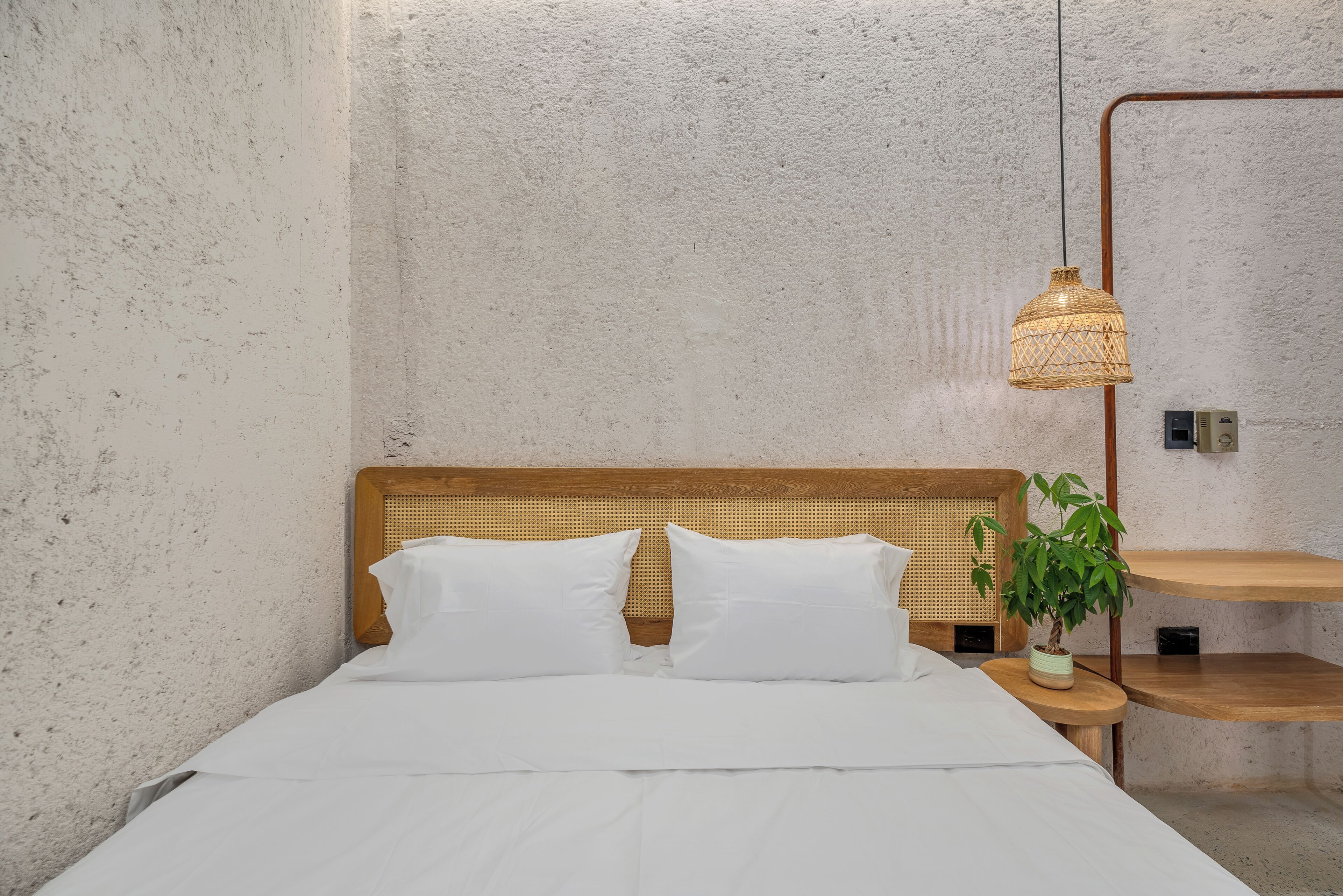 A bed with white bedding, a woven headboard, and a hanging light fixture.