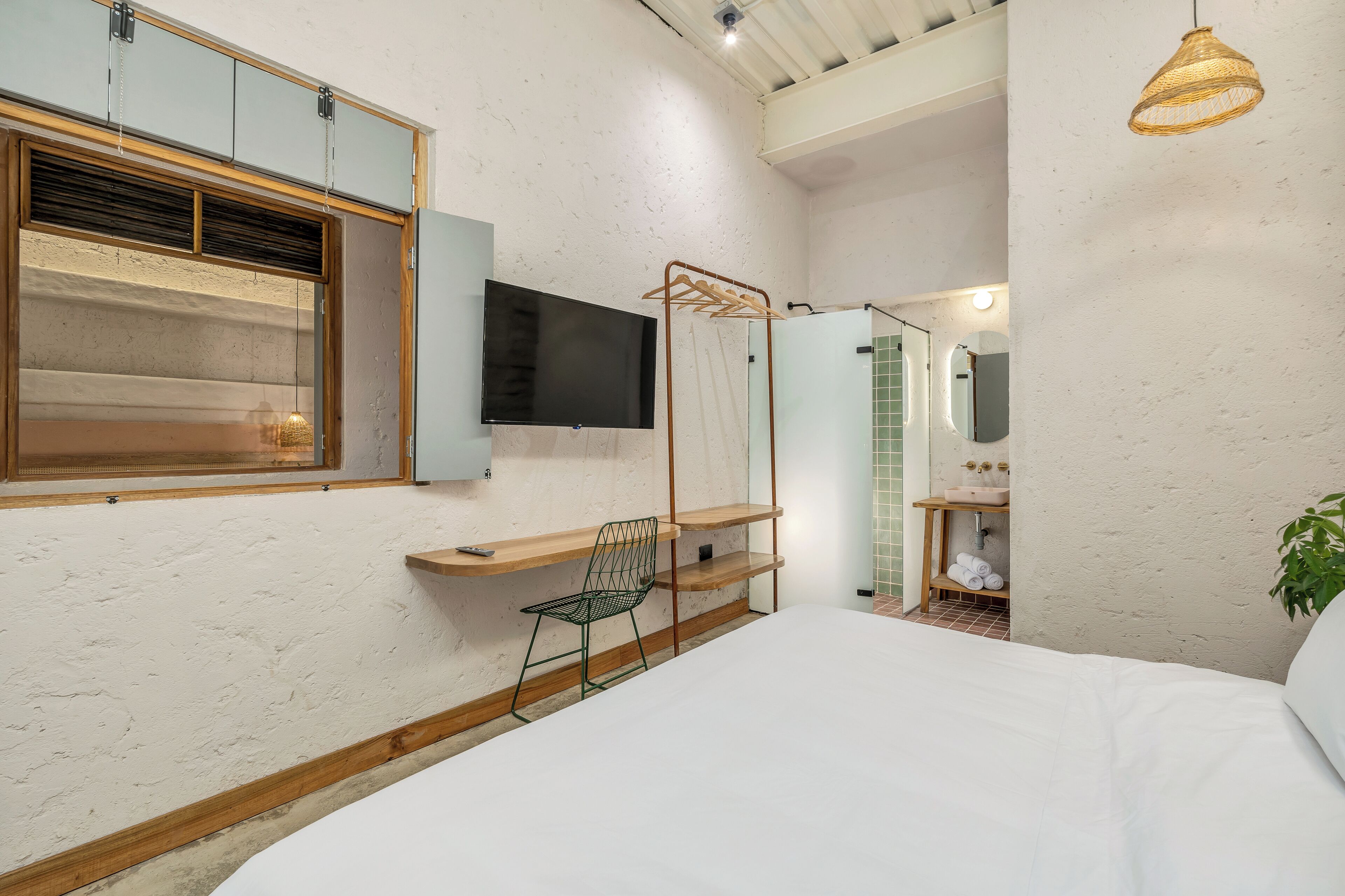 A bedroom with a bed, a TV, a wooden desk, a chair, and a hanging light fixture.