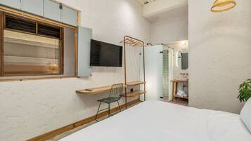A bedroom with a bed, a TV, a wooden desk, a chair, and a hanging light fixture.