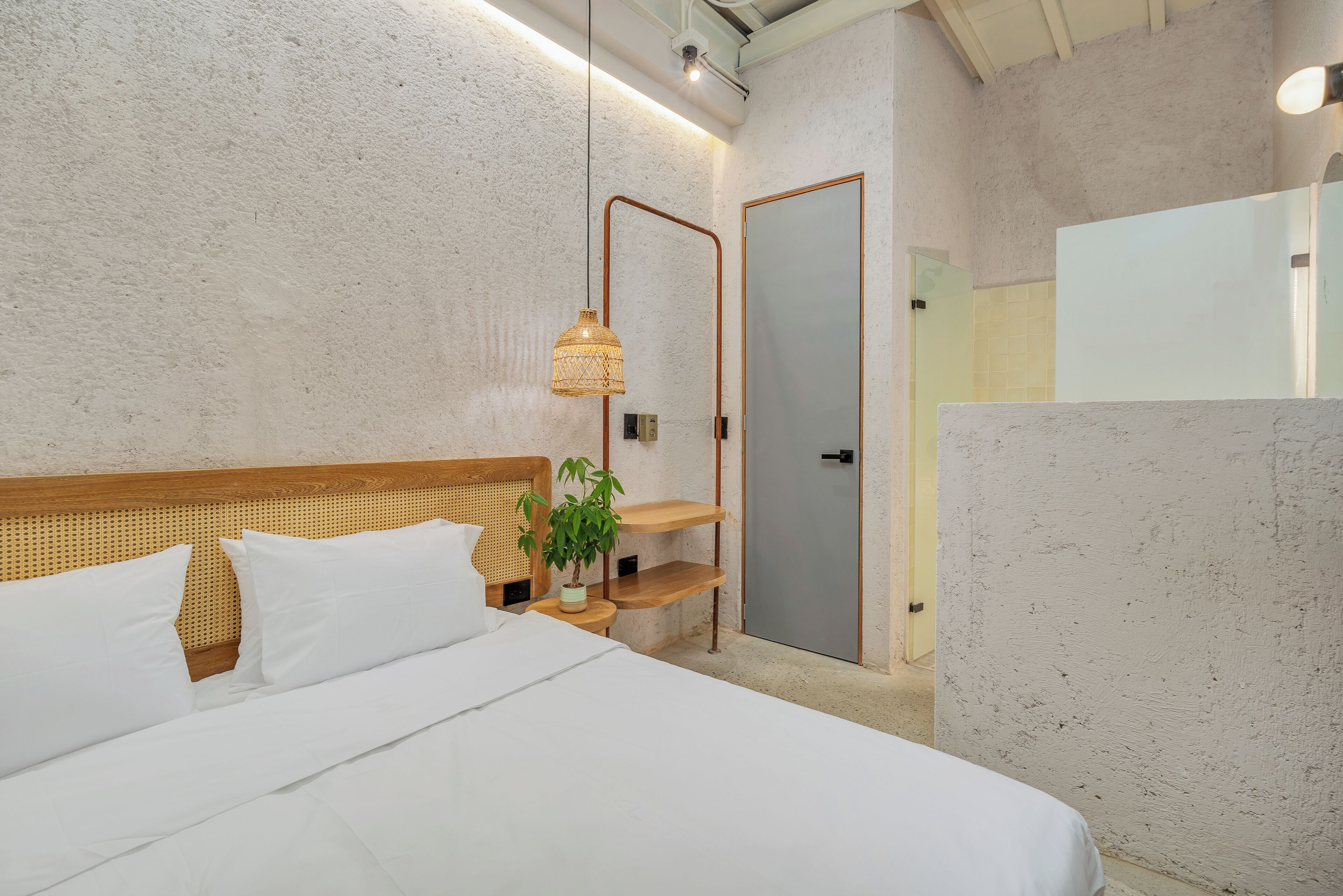 A bedroom with a wooden headboard, white bedding, a bedside plant, and a mirror on the wall.
