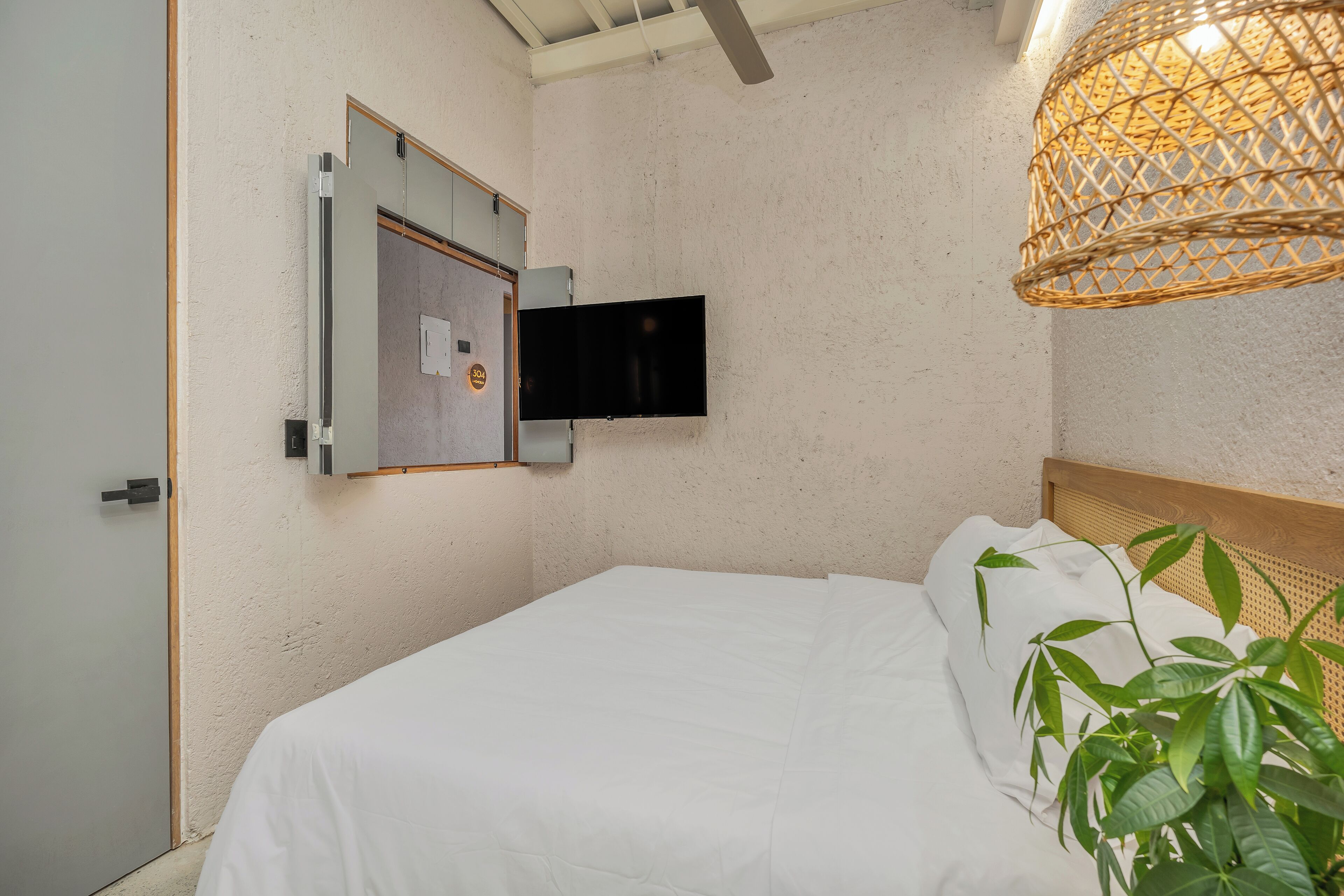 A bedroom with a bed, a mounted TV, and a hanging light fixture.