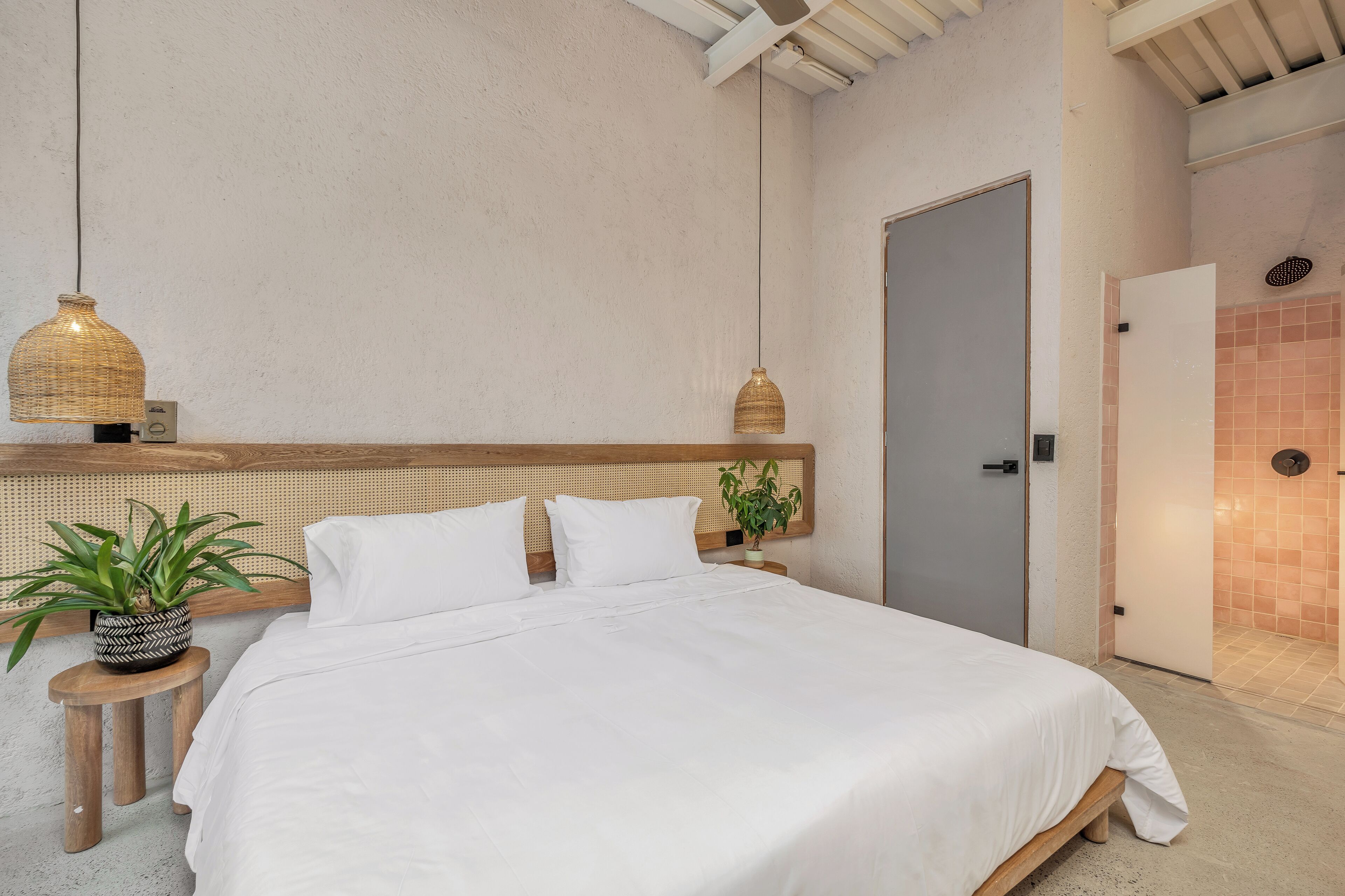 A neatly made bed with white linens, a woven headboard, and a hanging light fixture.