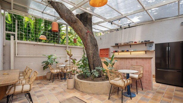 A spacious patio with a large tree, outdoor seating, and a kitchen area. - Botánica Manila by HOUSY HOST (Medellín)