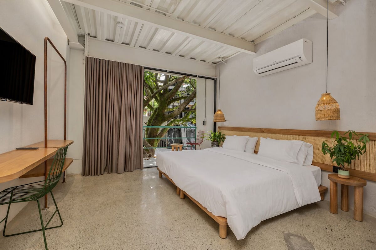 A bedroom with a bed, a desk, a chair, a TV, and an air conditioning unit.