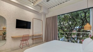 A bedroom with a large bed, a TV mounted on the wall, a chair, and a window with curtains. - Botánica Manila by HOUSY HOST (Medellín)