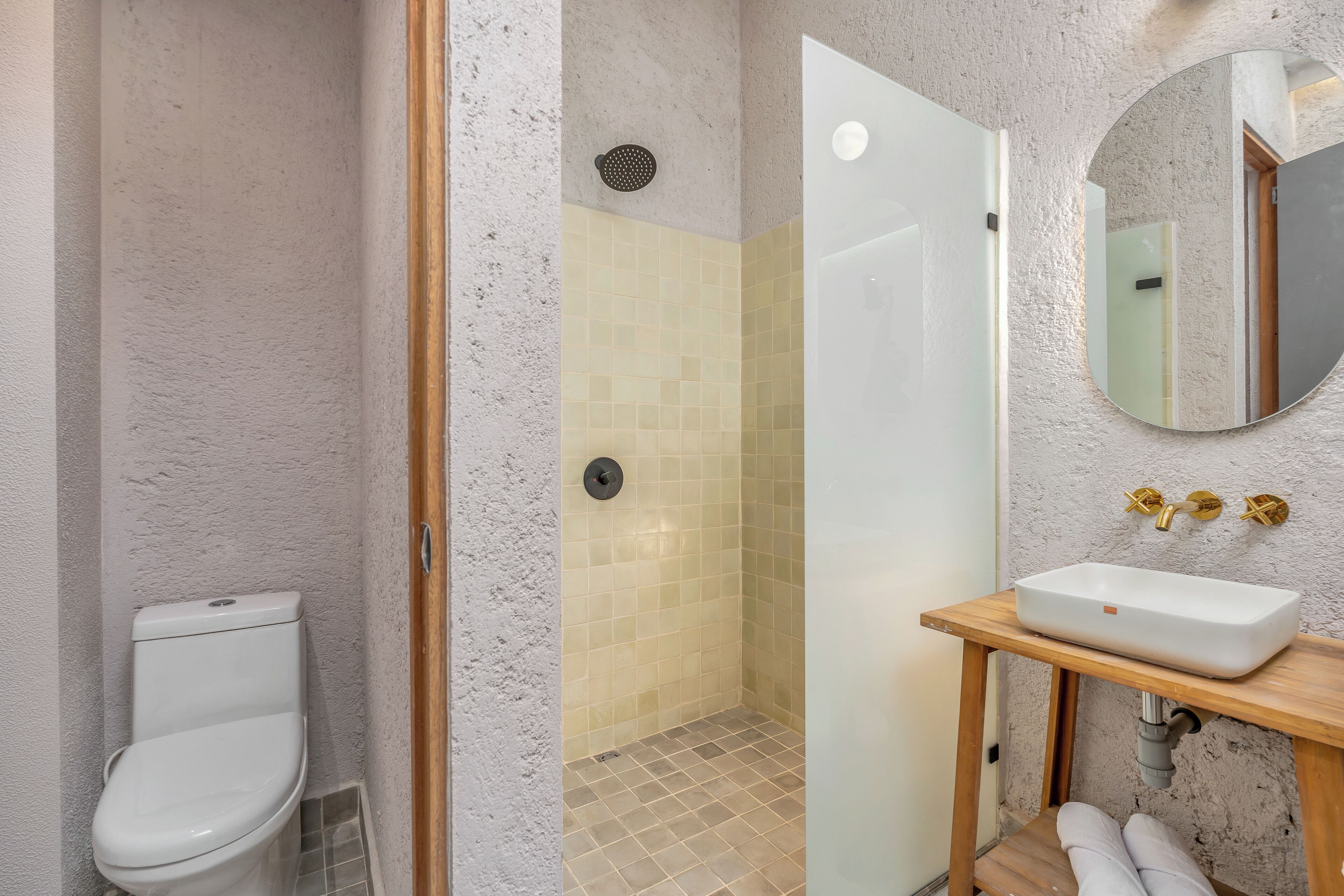 Une salle de bain comprenant des toilettes, une douche aux murs carrelés et un lavabo avec un miroir au-dessus.