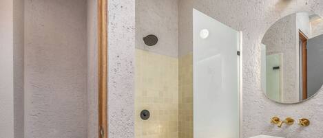 Une salle de bain comprenant des toilettes, une douche aux murs carrelés et un lavabo avec un miroir au-dessus.