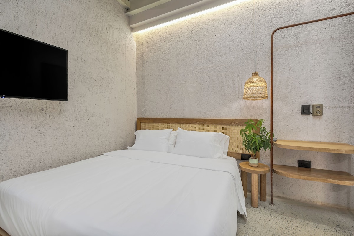 A bedroom with a bed, a mounted TV, a hanging light fixture, and wooden shelves.