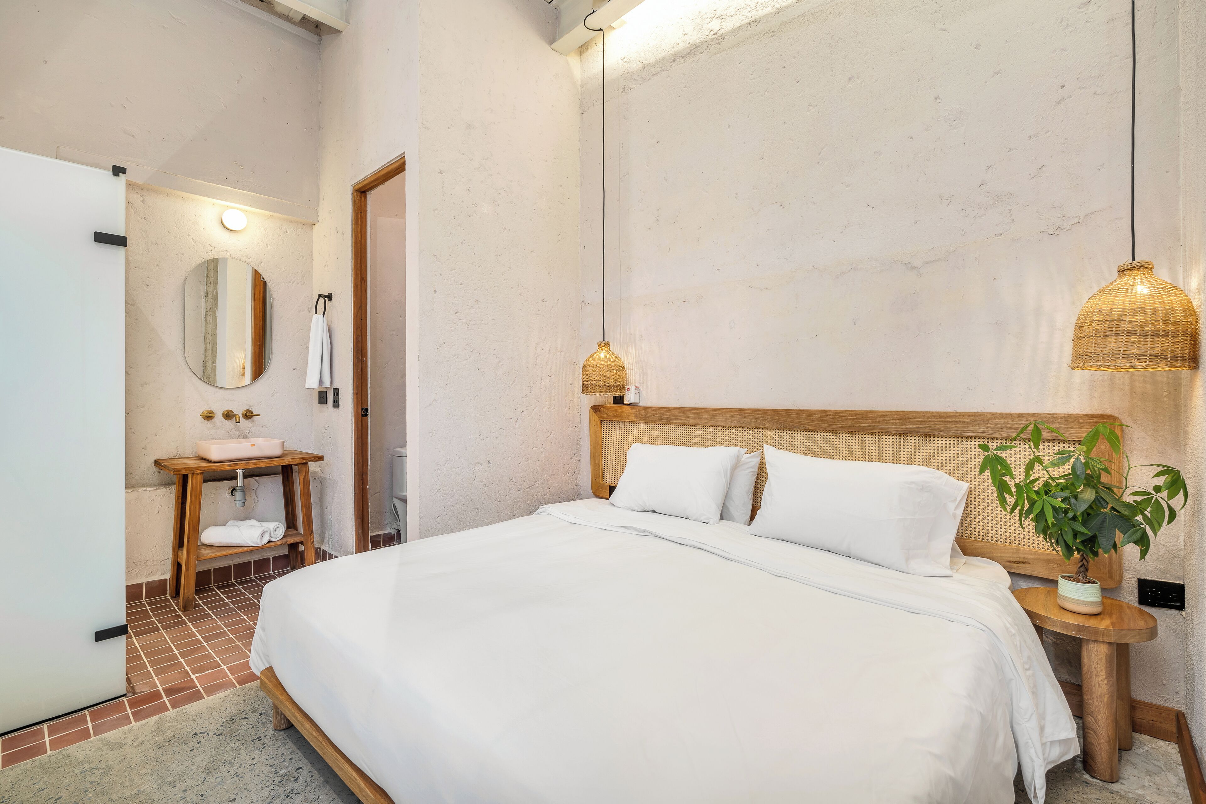 A bedroom with a bed, a bedside table, a mirror, a sink, and a hanging light fixture.
