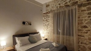 Un dormitorio con cama, ventilador de techo, pared de piedra, ventana con cortinas y piso estampado.