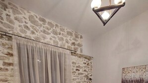 Una sala de estar con pared de piedra, un sofá gris con cojines estampados, una mesa de centro de madera y un cuadro en la pared.