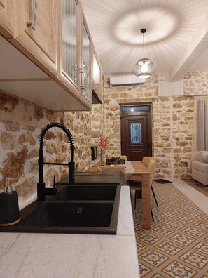 A kitchen with a stone wall, wooden cabinets, a black sink, and a dining area with a patterned rug. - Stone-built 80 m2 2bedroom villa in Preveza center with private garden & Parking (Preveza)