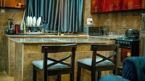 Une cuisine dotée d’un îlot central, de deux tabourets de bar, d’une cuisinière et d’une fenêtre avec des rideaux.