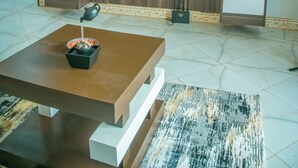 Un salon moderne avec un grand téléviseur à écran plat fixé sur un mur en bois, une table basse sur laquelle se trouve un saladier rempli de fruits et un tapis à motifs.