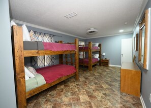 Ein Zimmer mit drei Etagenbetten, einem kleinen Nachttisch aus Holz und einem Spiegel an der Wand.