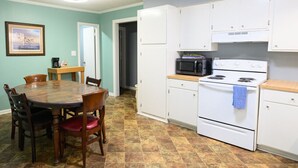 Une cuisine compacte avec des meubles blancs, une cuisinière et un four à micro-ondes. On y trouve une table à manger avec des chaises et un tableau encadré accroché au mur.