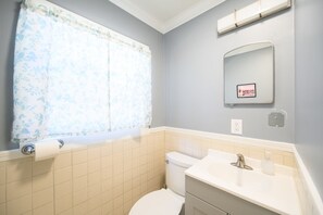 Un baño con inodoro, lavamanos y ventana con cortina estampada.