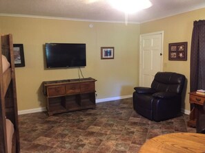 Una sala de estar con un televisor de pantalla plana montado en la pared, un sillón de cuero, un mueble de madera y una puerta.