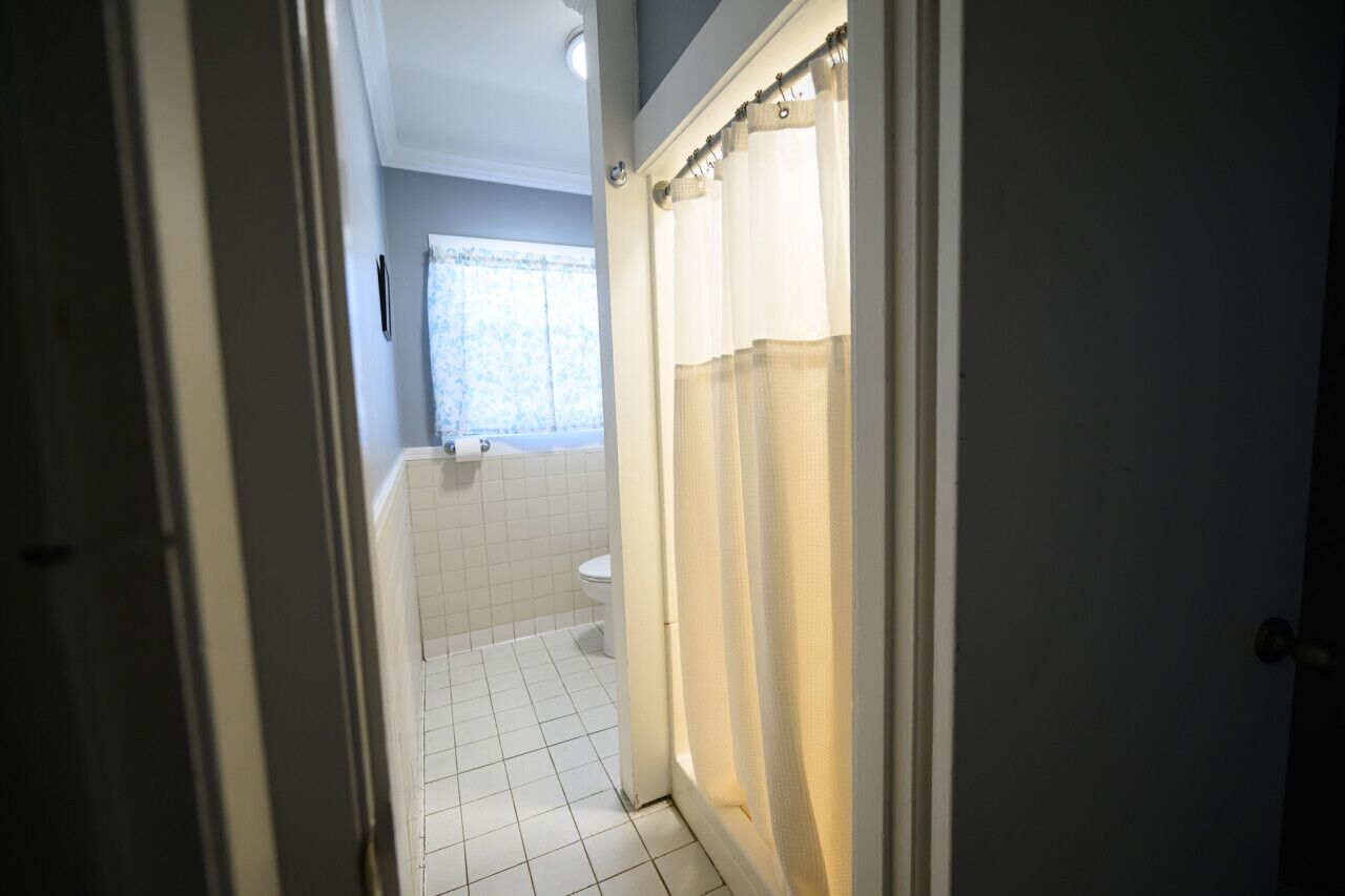 A bathroom with white tiles, a toilet, and a shower curtain.