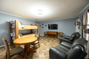 A cozy living room with a bunk bed, a dining table, and a leather sofa. - Fishing cabin with views on Lake Chicot! (Lake Village)
