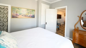 A bedroom with a bed, a dresser, a painting, and a door leading to another room. - Watch the sunrise with your family on Lake Chicot! (Lake Village)