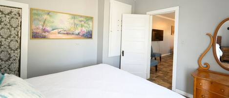 A bedroom with a bed, a dresser, a painting, and a door leading to another room.