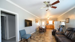 A living room with a sofa, a chair, a dining table with chairs, a ceiling fan, and a kitchen in the background. - Watch the sunrise with your family on Lake Chicot! (Lake Village)