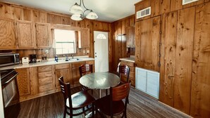 Une cuisine avec des meubles de rangement en bois, un four à micro-ondes, un grille-pain, un évier et une table à manger avec des chaises.
