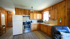 A compact kitchen with wooden cabinets, a refrigerator, an oven, a microwave, and a sink.
