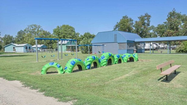 Een speeltuin met groene tunnels, een schommel en een picknicktafel.