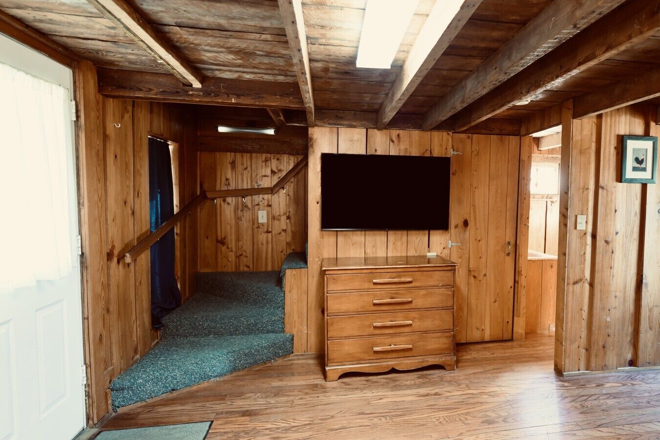 Un intérieur en bois avec un escalier, un téléviseur à écran plat fixé au mur et une commode en bois.