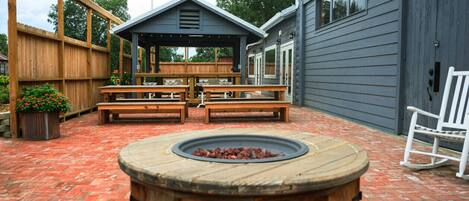 A patio with a wooden fire pit, wooden benches, and a covered seating area.