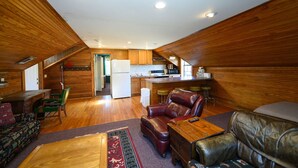 Amplia sala de estar con chimenea, asientos de cuero y una zona de cocina con armarios de madera y refrigerador.