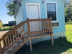 Una casa pequeña de azul claro con una escalera de madera que lleva a la puerta principal.