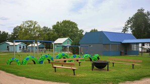 Une aire de jeux avec des balançoires faites de pneus verts et bleus, des tables de pique-nique et un bâtiment doté d’un toit bleu.