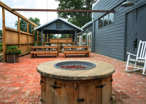 A patio with a wooden fire pit, wooden benches, and a covered seating area.